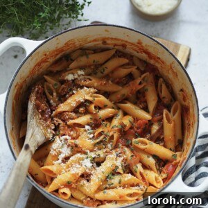 Penne with sausage ragu and grated cheese in a white casserole dish.