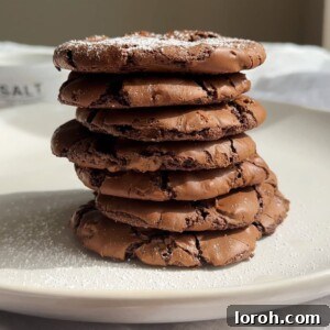 A stack of perfectly baked chocolate brownie cookies with crinkly tops on a white plate, ready to be enjoyed.