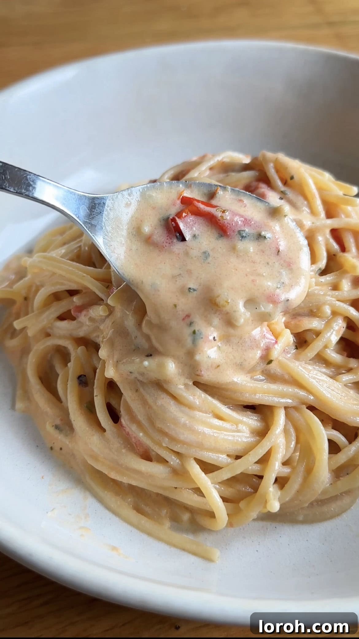 A serving of creamy Boursin tomato pasta being spooned onto a plate, showcasing the rich sauce and fresh basil garnish.