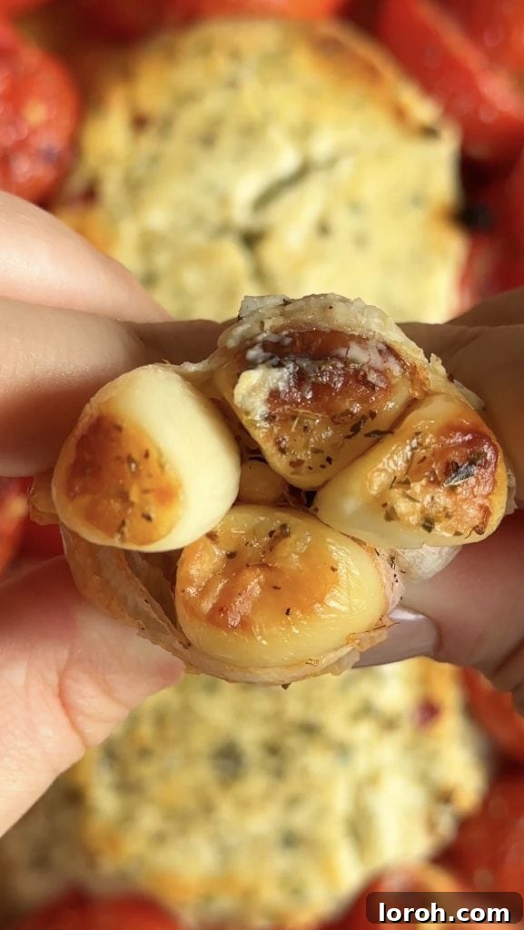 A woman's hand squeezing a head of roasted garlic, allowing the soft, mellow cloves to pop out into the roasting dish.