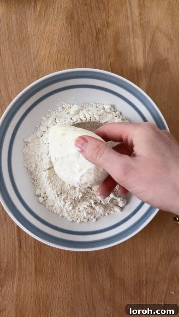 Crispy Mozzarella, Prosciutto, and Marinara Sandwich 5 A person carefully coating a ball of fresh mozzarella in a bowl of seasoned flour, ensuring an even layer.