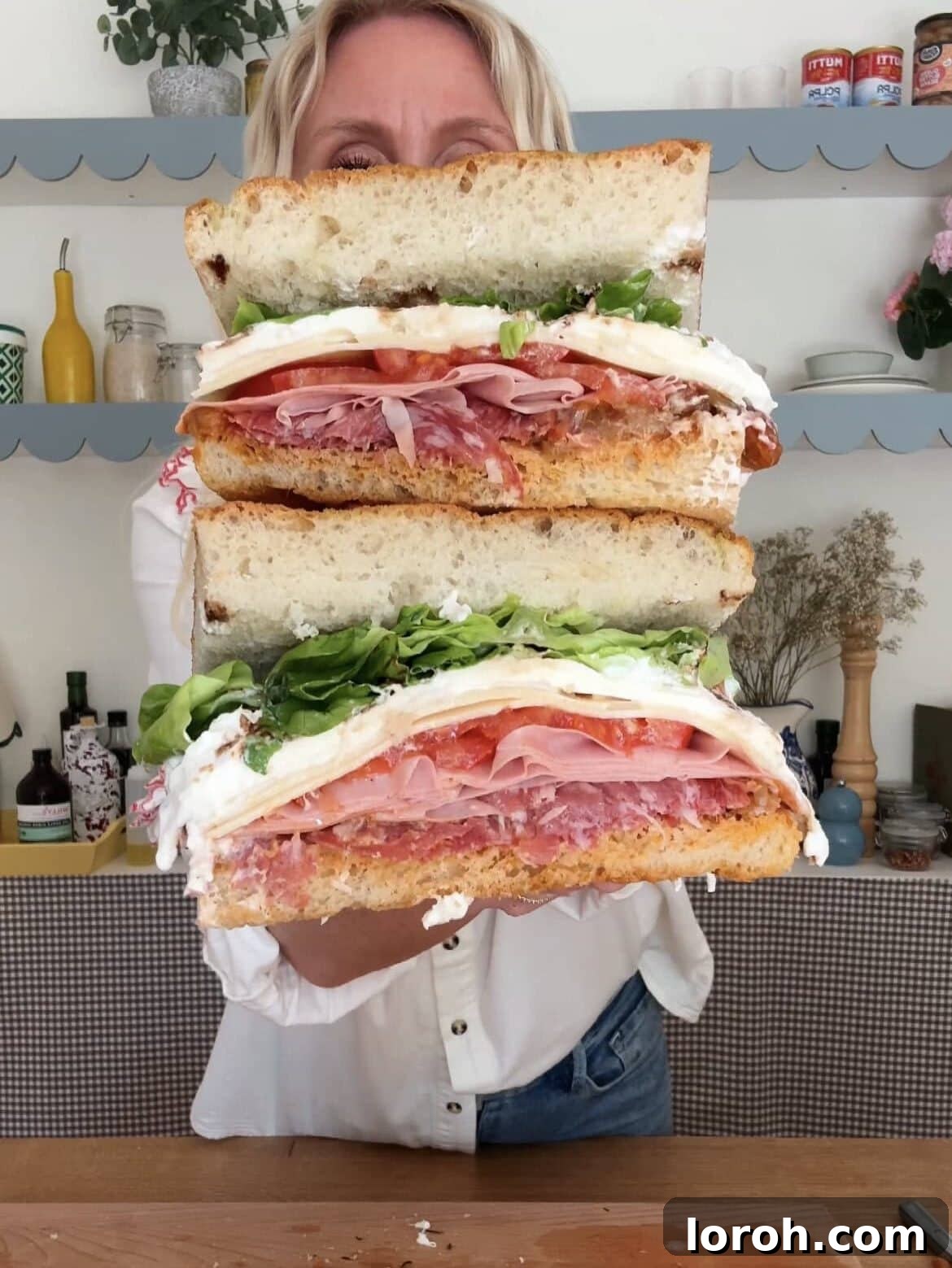A woman holding a beautifully assembled Burrata and Salami Focaccia Sandwich with Aubergine Caponata, showcasing its rich layers and appealing presentation.