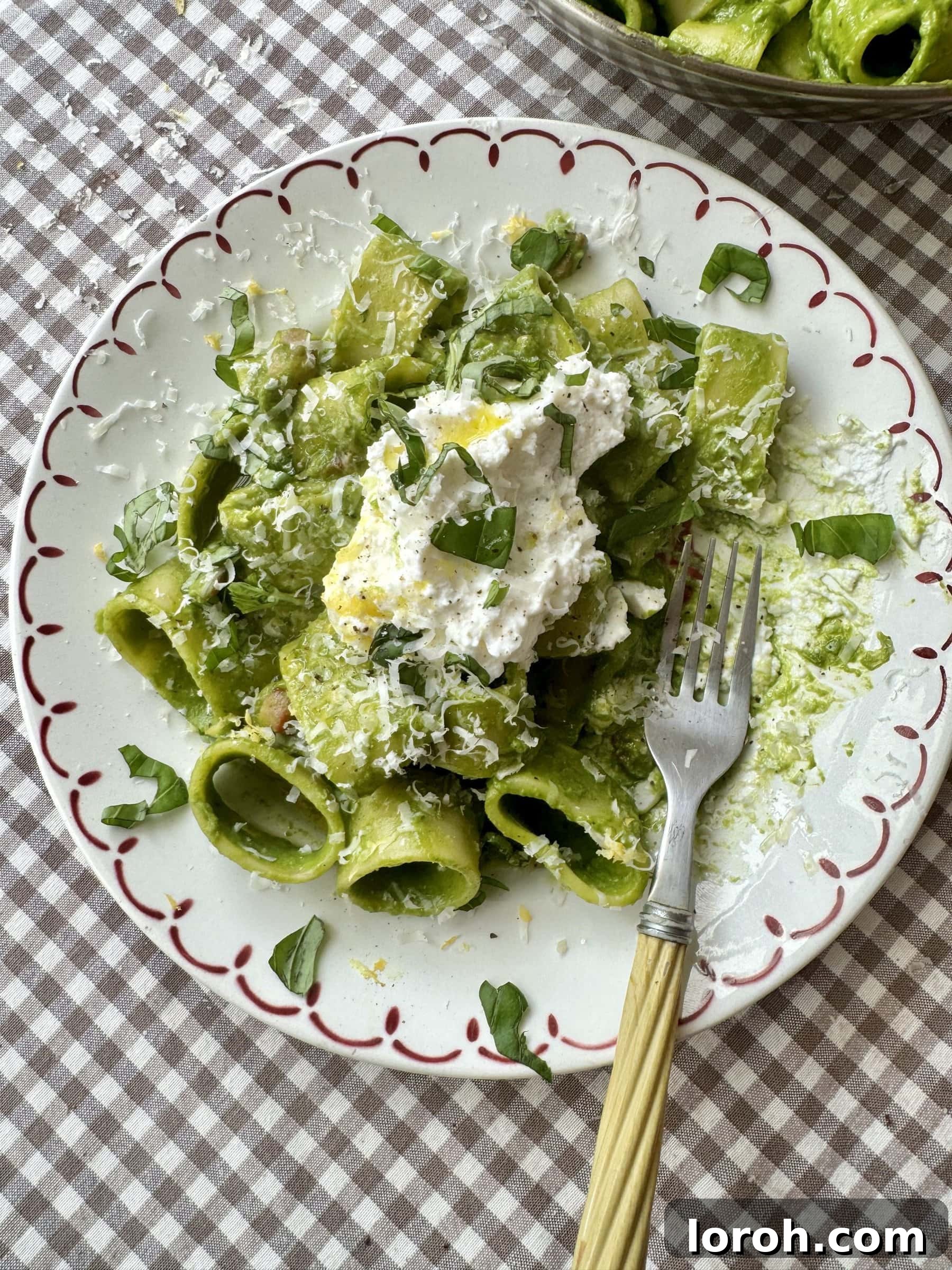A plate of pasta in green sauce, beautifully topped with grated cheese, ready to be enjoyed.