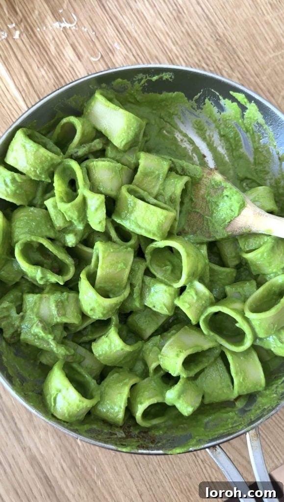 The finished pasta in green sauce, presented beautifully in a gleaming silver frying pan, showcasing its rich texture.