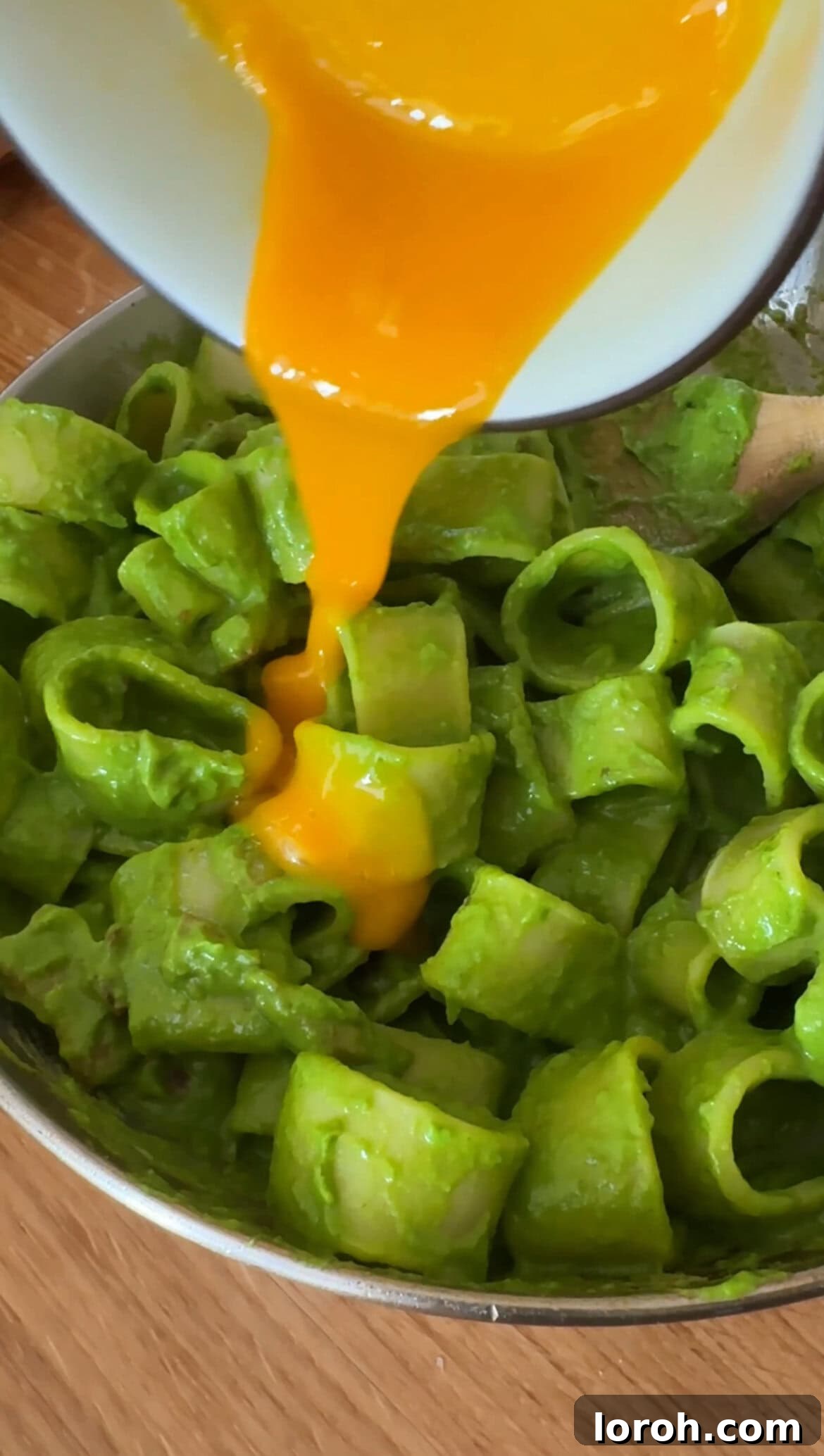 The whisked egg yolk being added to the pasta and green sauce in the pan, for a glossy finish.