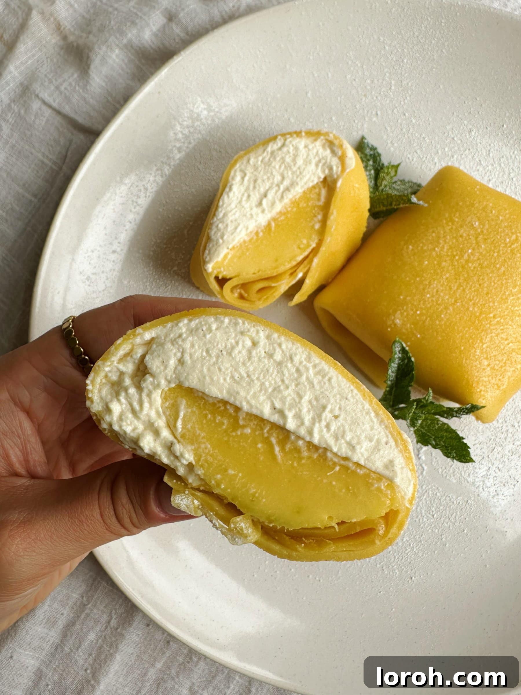 woman holding a mango pancake on a white plate, showcasing the vibrant filling