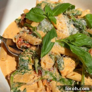 A close-up shot of creamy Marry Me Pasta in a white bowl, garnished with basil, ready to be served.