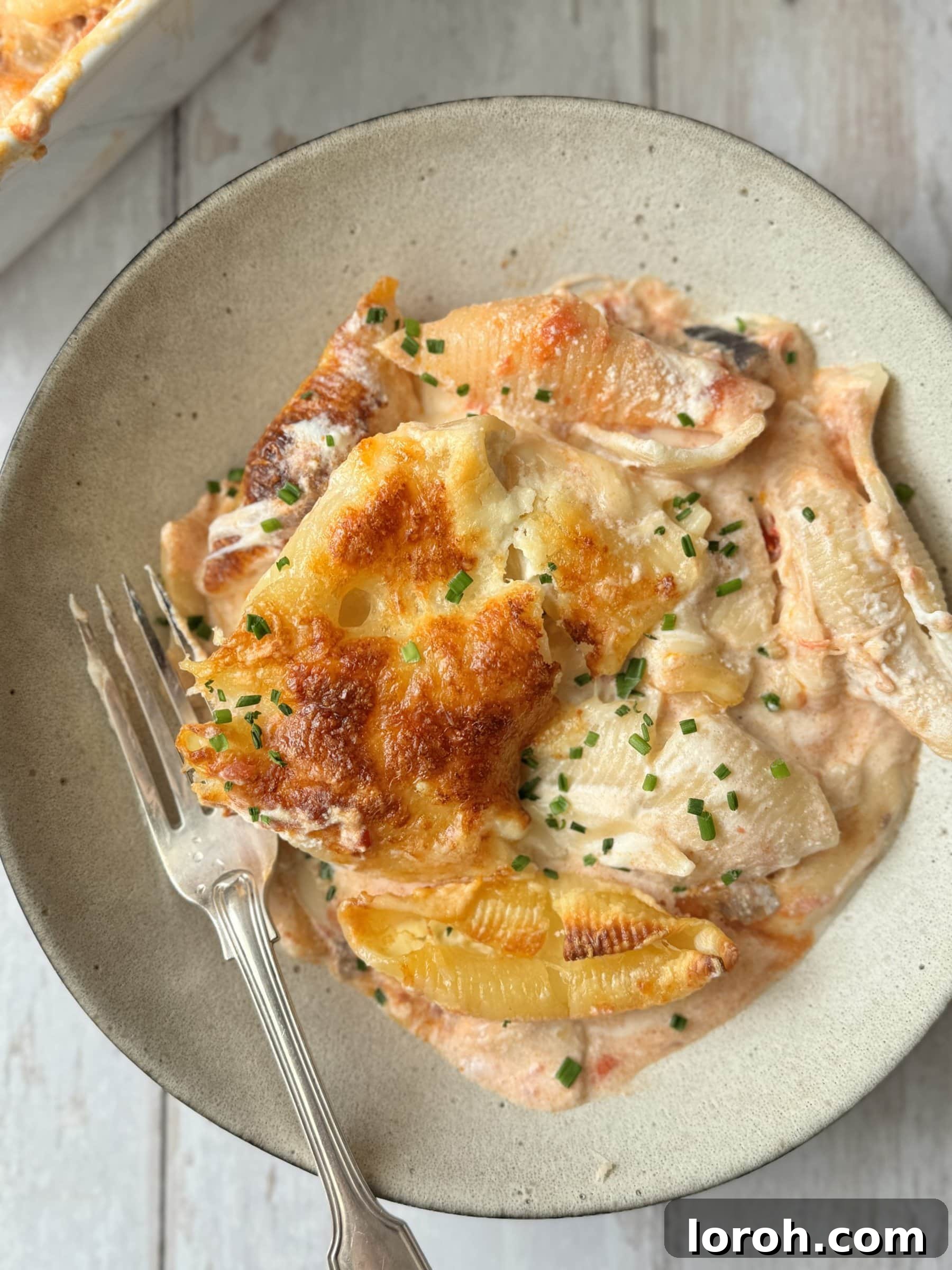 A bowl of creamy ricotta and aubergine giant shell pasta bake, garnished with fresh basil.