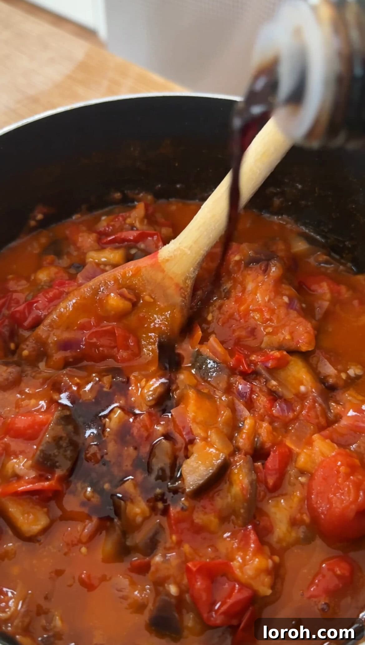 Adding cherry tomatoes, canned tomatoes, and water to the pan with aubergine and onion for the sauce.