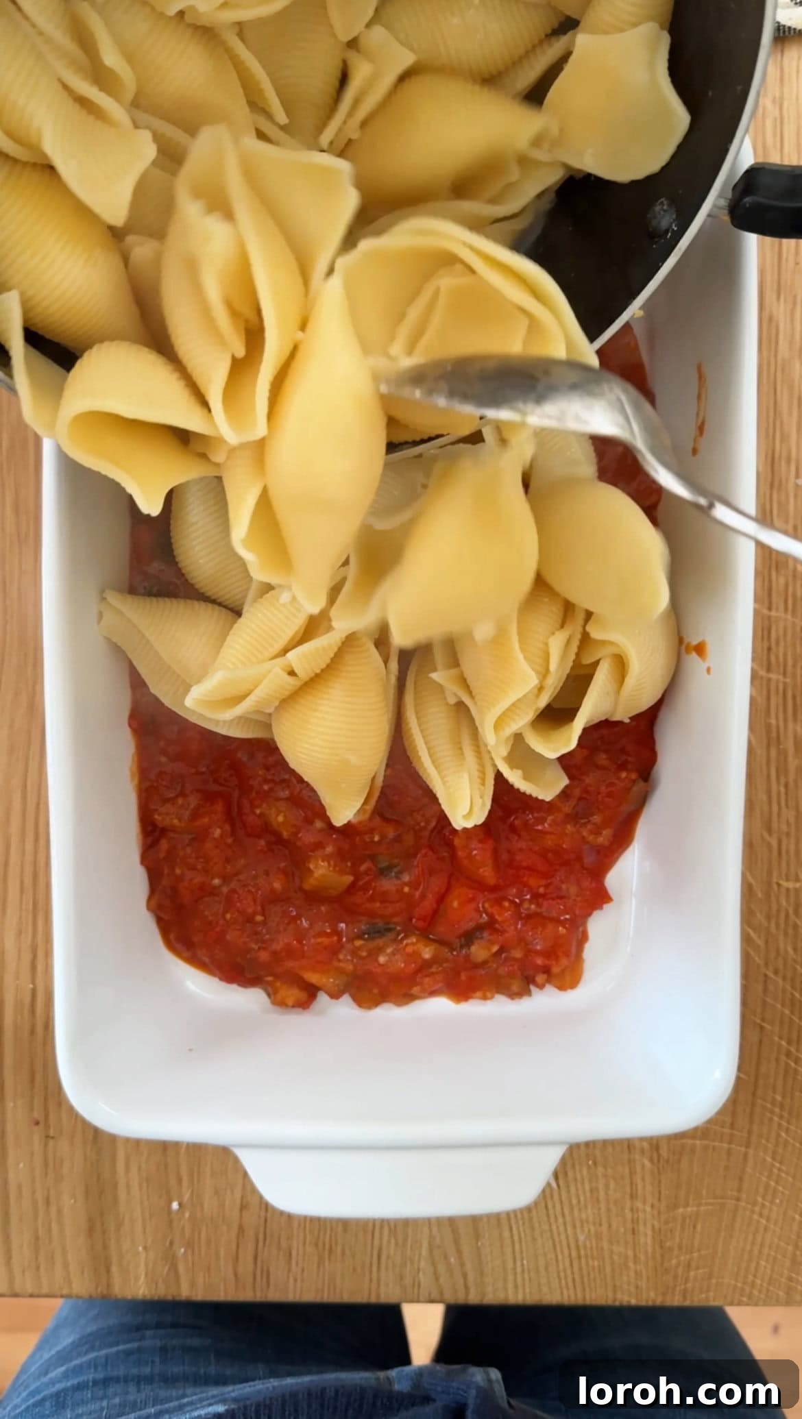 Layering giant shell pasta into a baking dish over a base of tomato sauce.