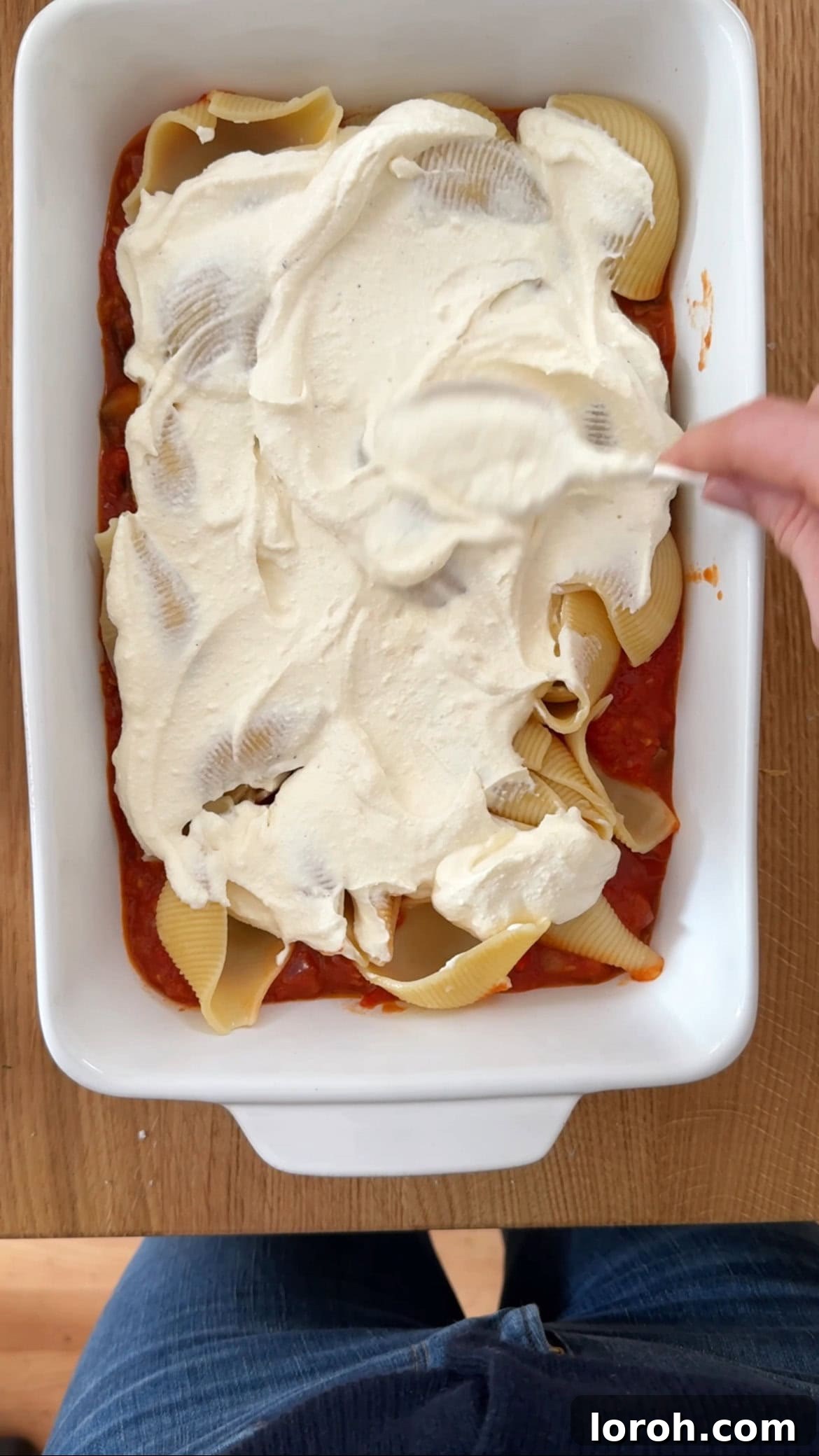 Spreading creamy ricotta sauce over a layer of giant shell pasta in the baking dish.