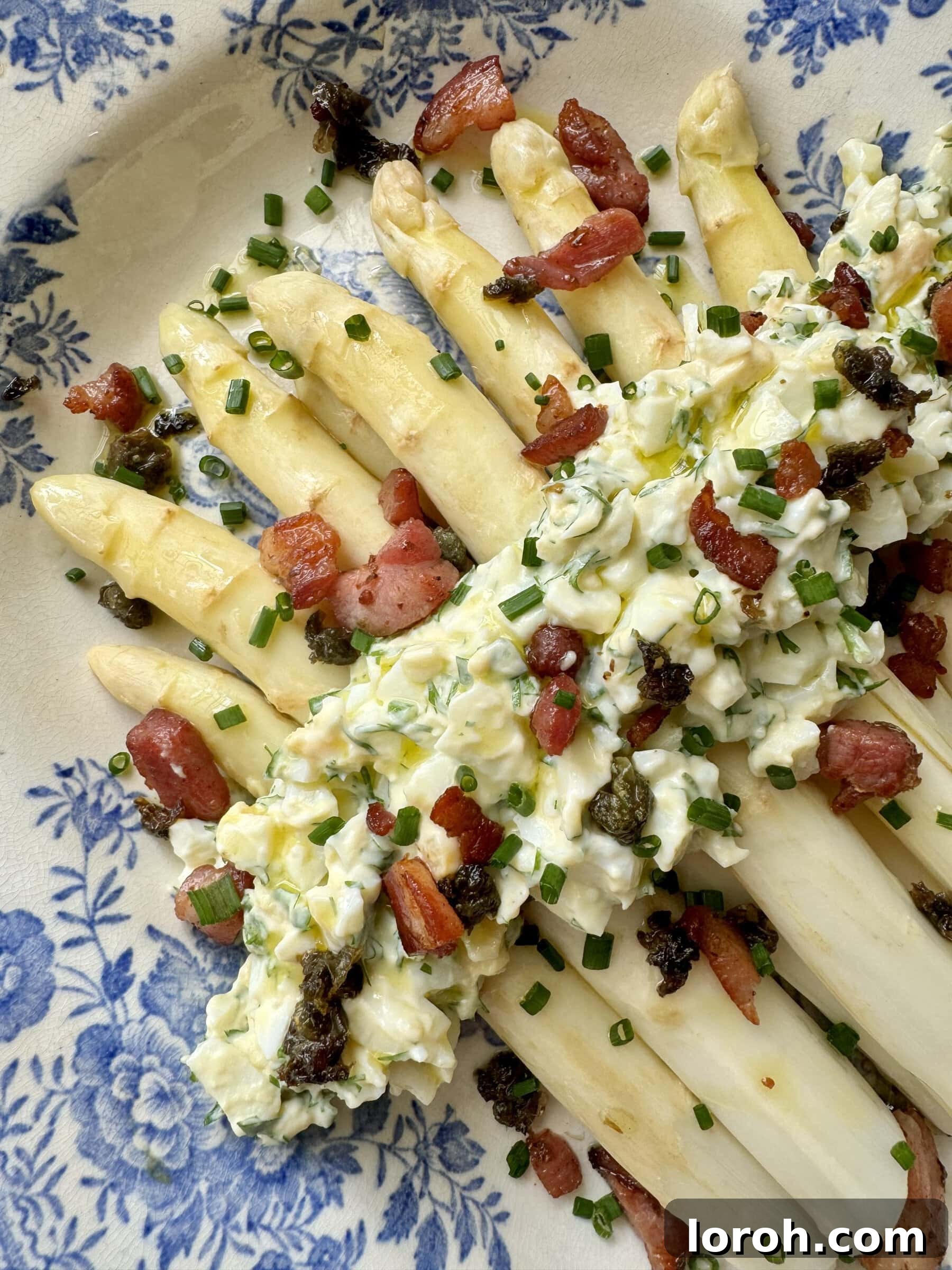 white asparagus topped with bacon on blue and white plate