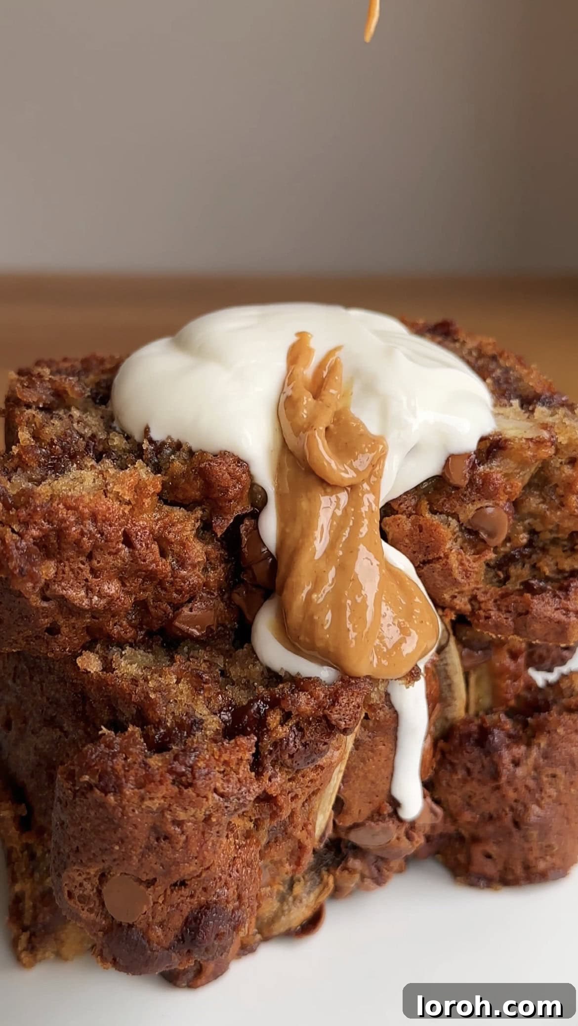 A spoon of yogurt and peanut butter on slices of decadent brown butter chocolate chip banana bread, showcasing its moist texture and melty chocolate.