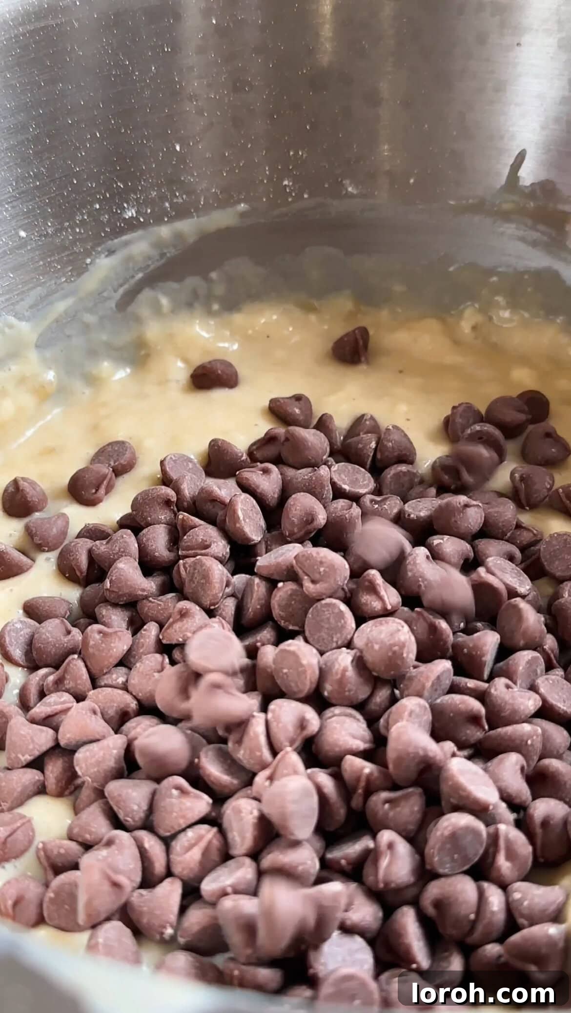 Folding dark chocolate chips into the banana bread batter with a spatula.