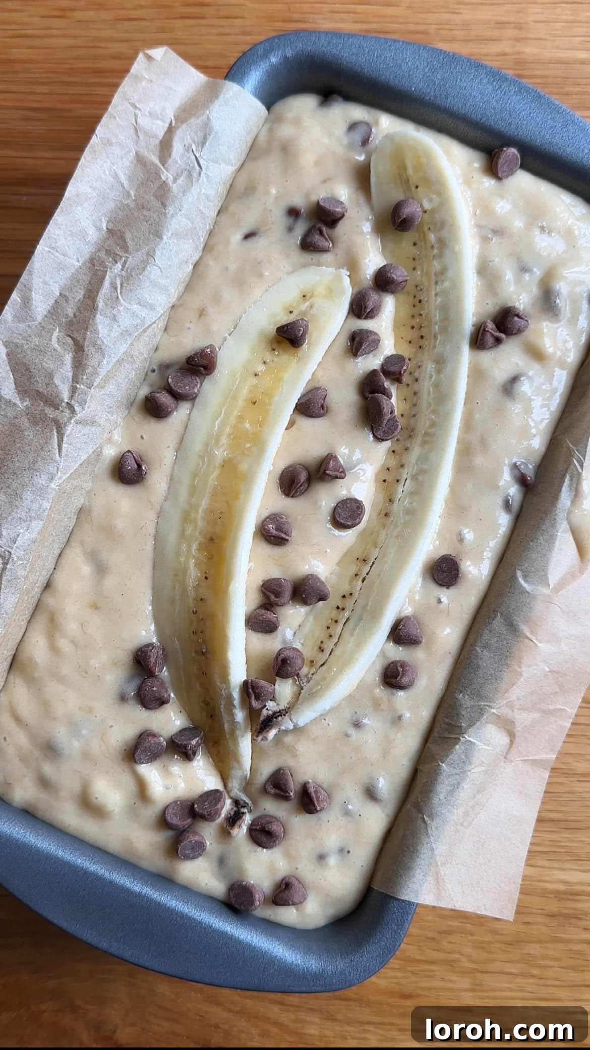 Topping the banana bread batter in the loaf pan with banana slices and extra chocolate chips before baking.