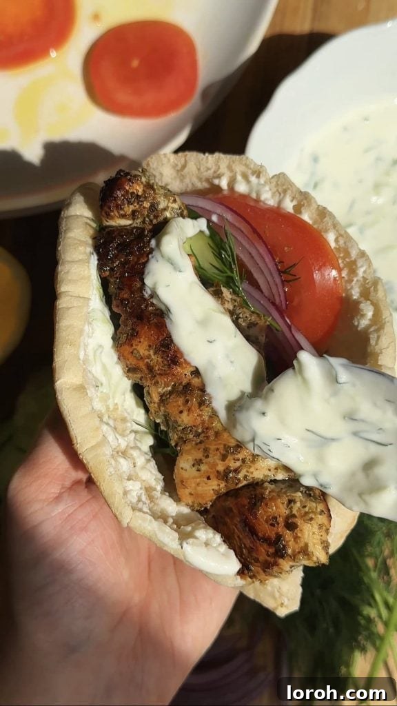 Spooning creamy tzatziki onto a chicken souvlaki pita with fresh vegetables
