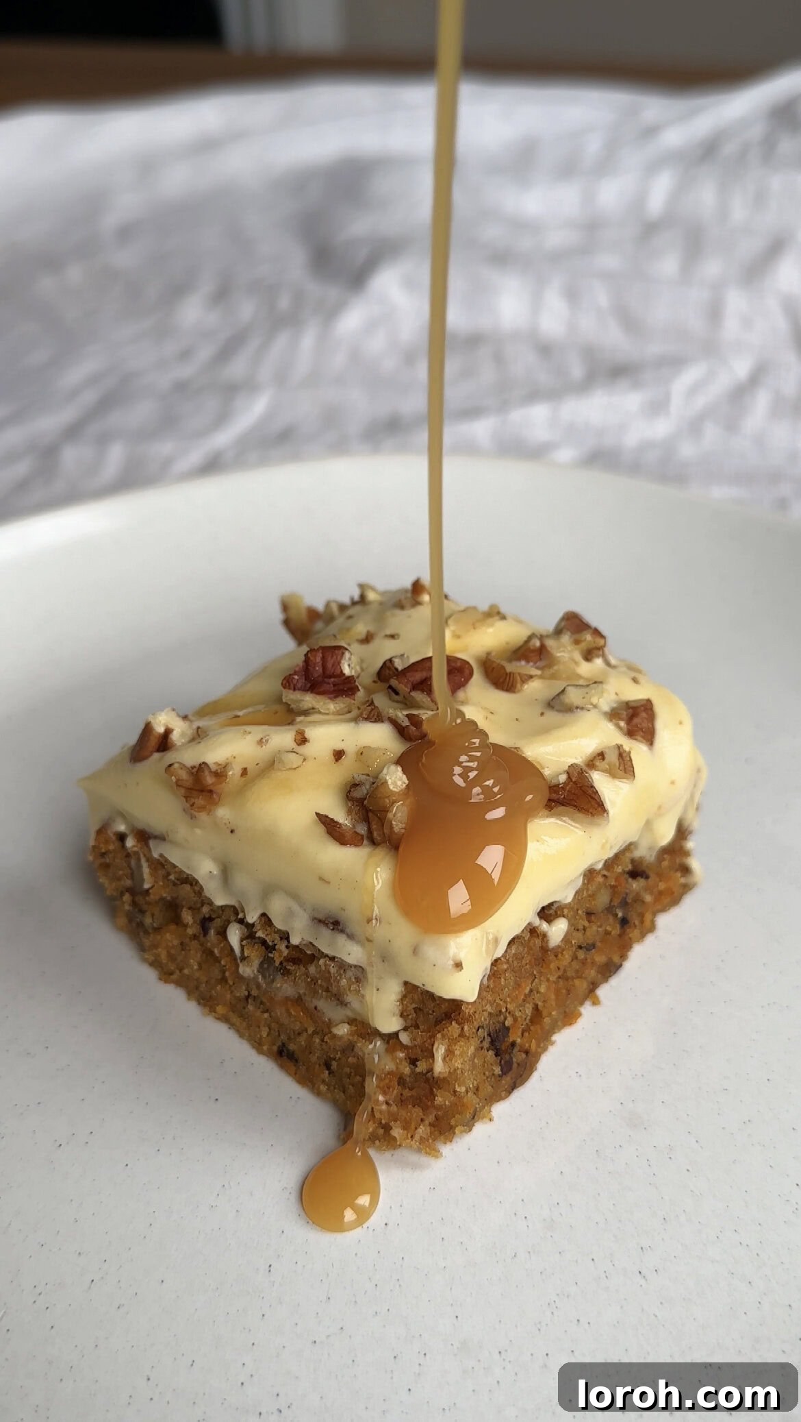 A delectable slice of carrot cake tray bake, generously drizzled with rich caramel sauce, invitingly presented.