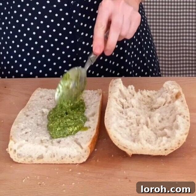 Spreading basil pesto generously onto a slice of crusty bread.