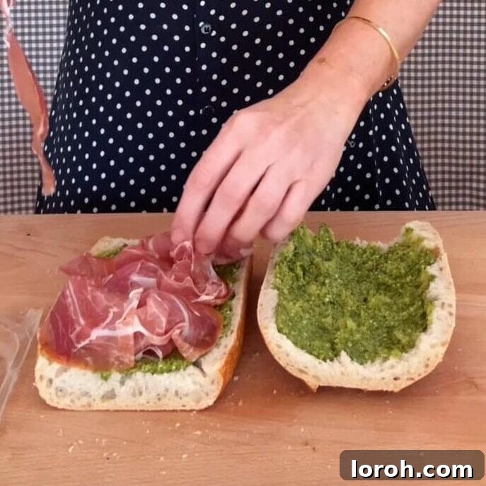 Arranging prosciutto slices in elegant curls on the pesto-coated bread.