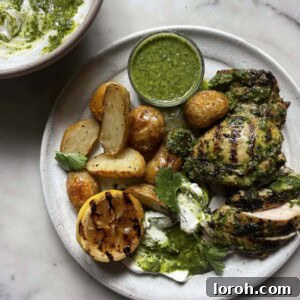 Zingy Grilled Chimichurri Chicken with Roasted Potatoes on a grey plate with a bowl of chimichurri yoghurt behind