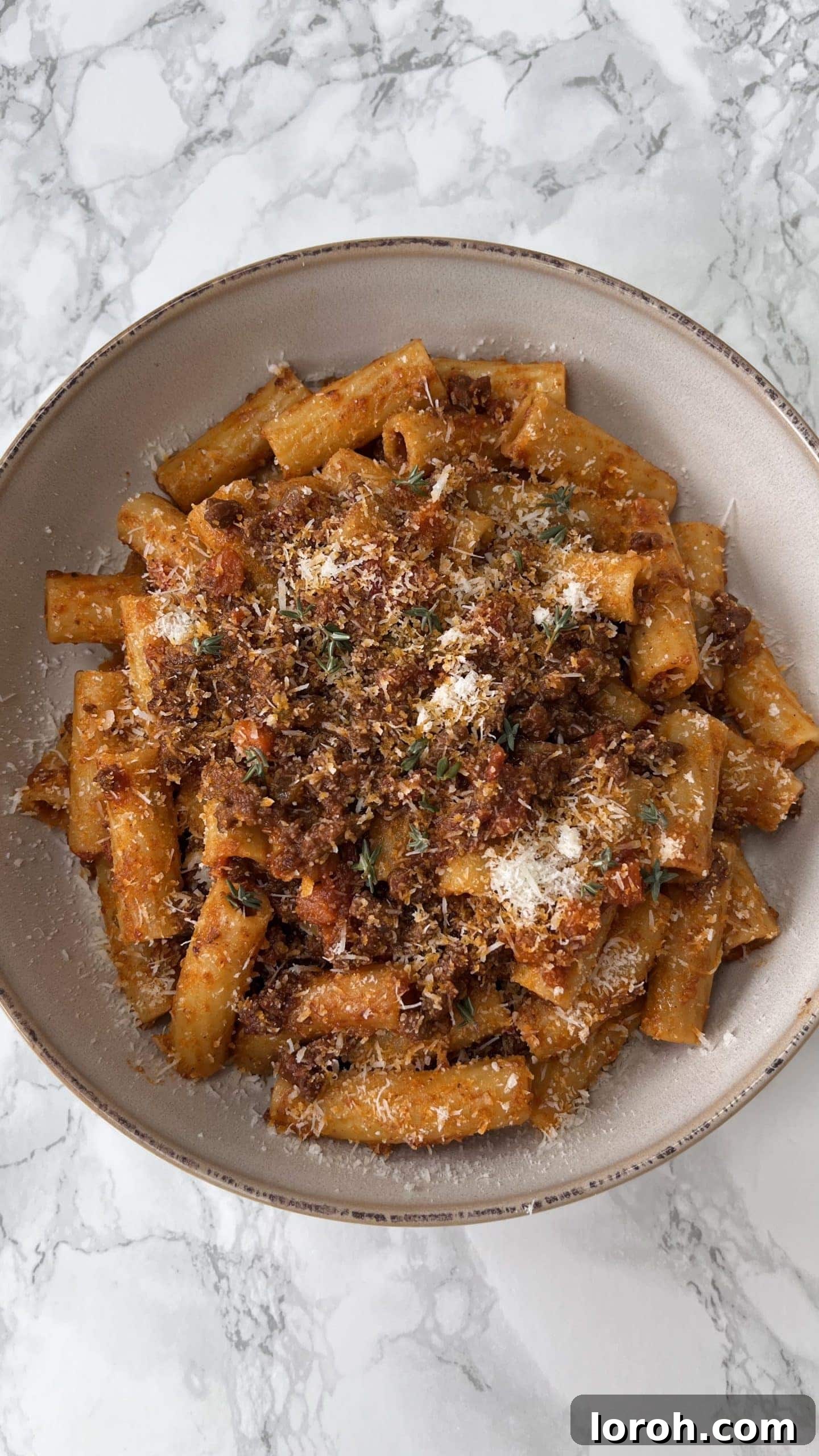 A beige bowl filled with hearty quick Bolognese sauce and rigatoni pasta, garnished and ready to be enjoyed.