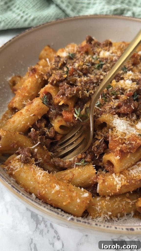 A fork lifts rigatoni coated in quick Bolognese sauce from a serving bowl, highlighting the sauce's texture.