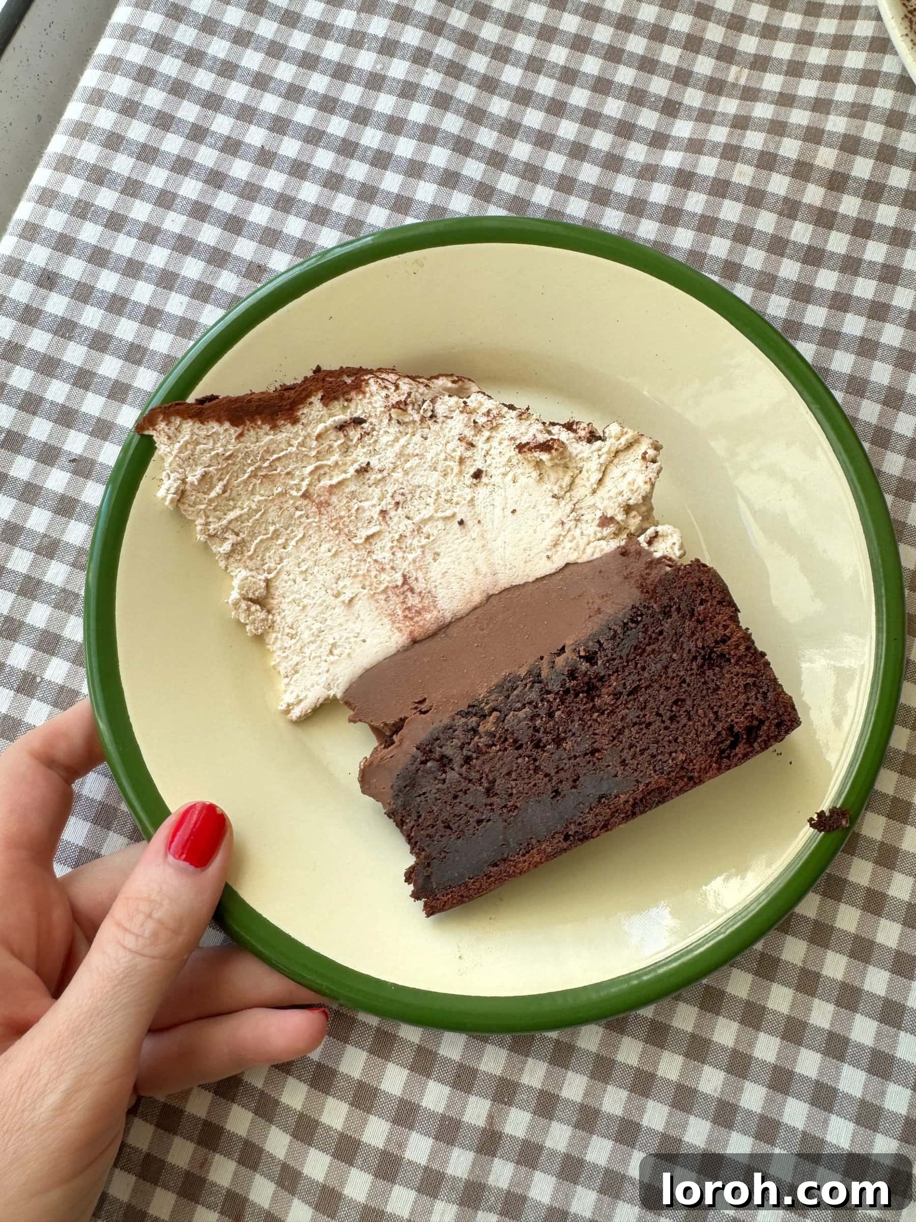 An inviting slice of chocolate mud cake, generously topped with malted whipped cream, resting on a green plate, highlighting its rich, moist layers.