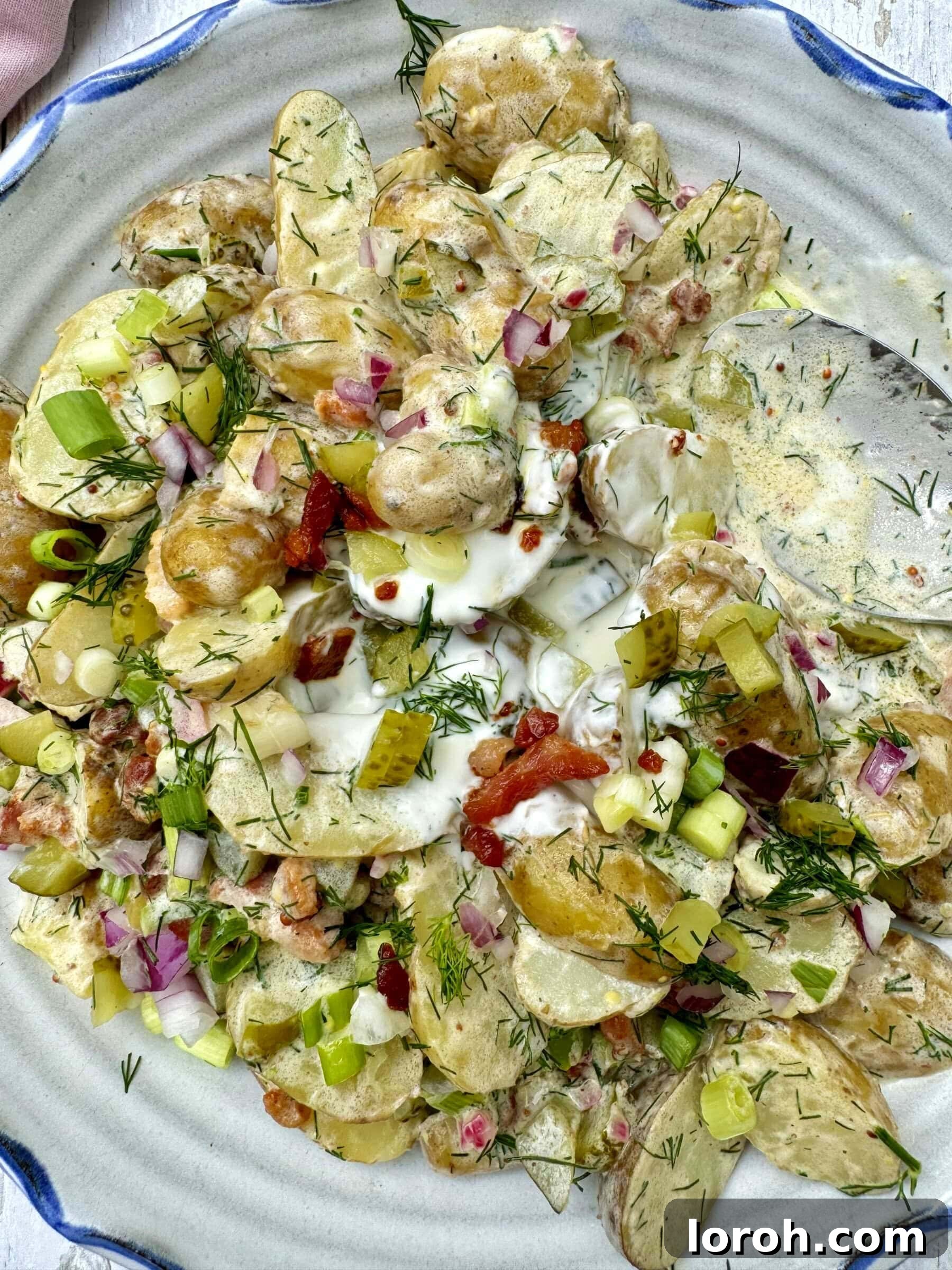 A serving bowl of creamy dill pickle potato salad with crispy pancetta, garnished with fresh dill.