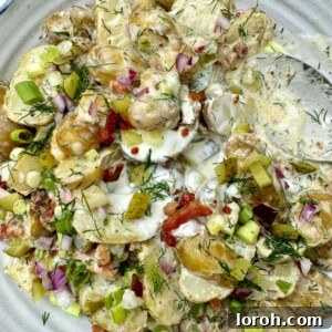 Serving bowl of creamy dill pickle potato salad with fresh dill and a spoon.