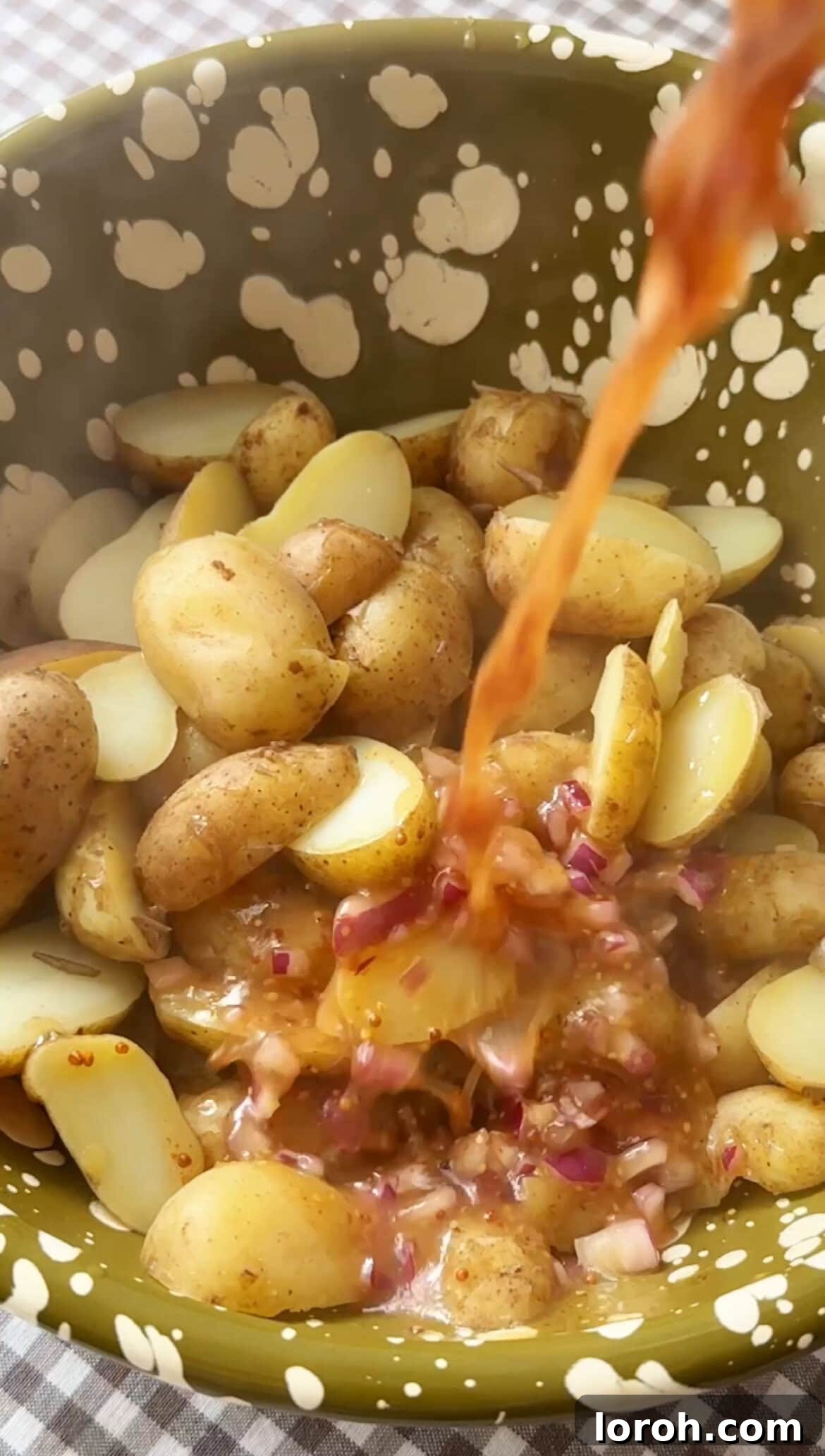 Pouring vinaigrette dressing over hot, drained potatoes in a mixing bowl.