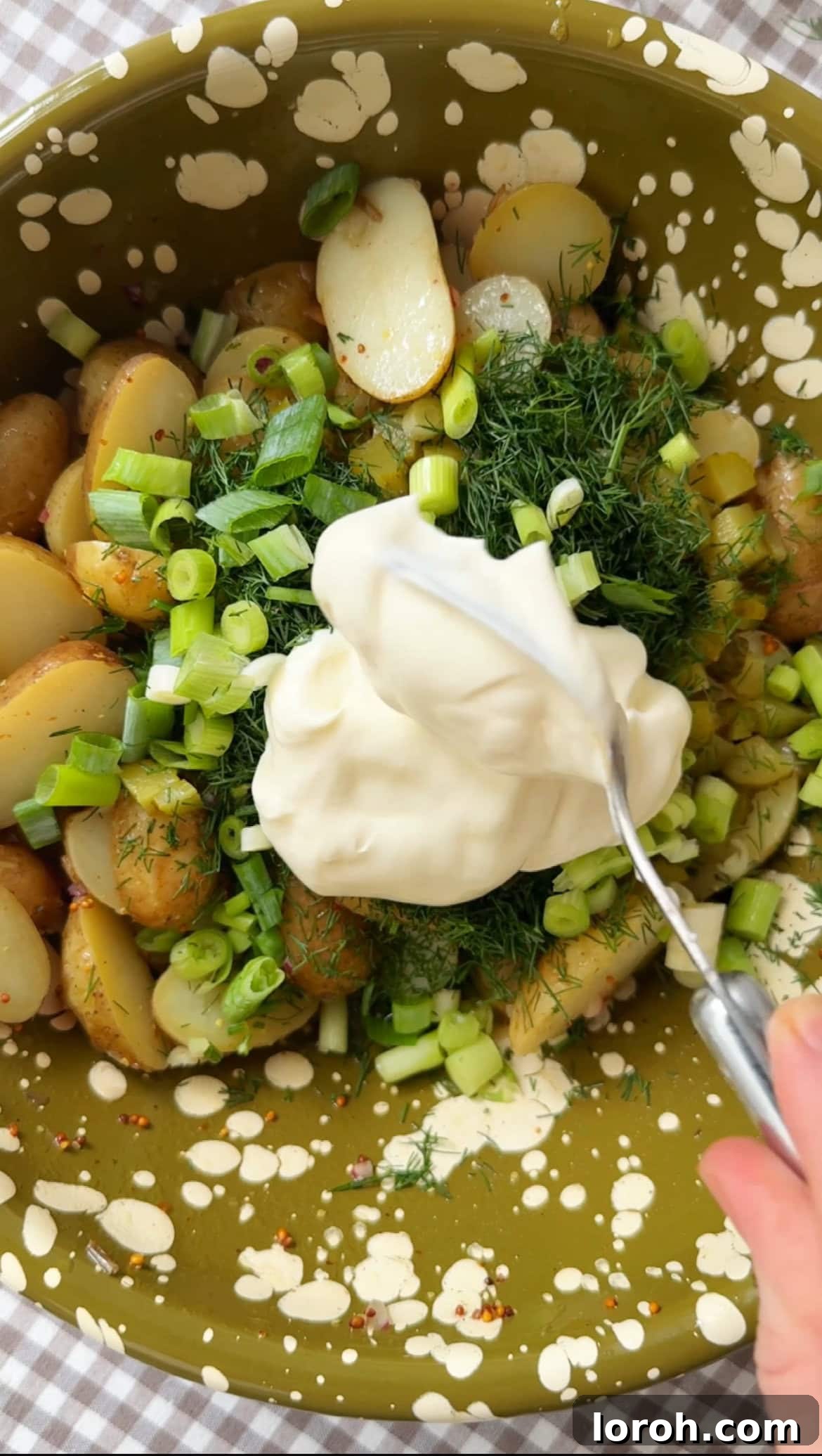 Mixing creme fraiche, mayonnaise, and chopped herbs into the potato salad.