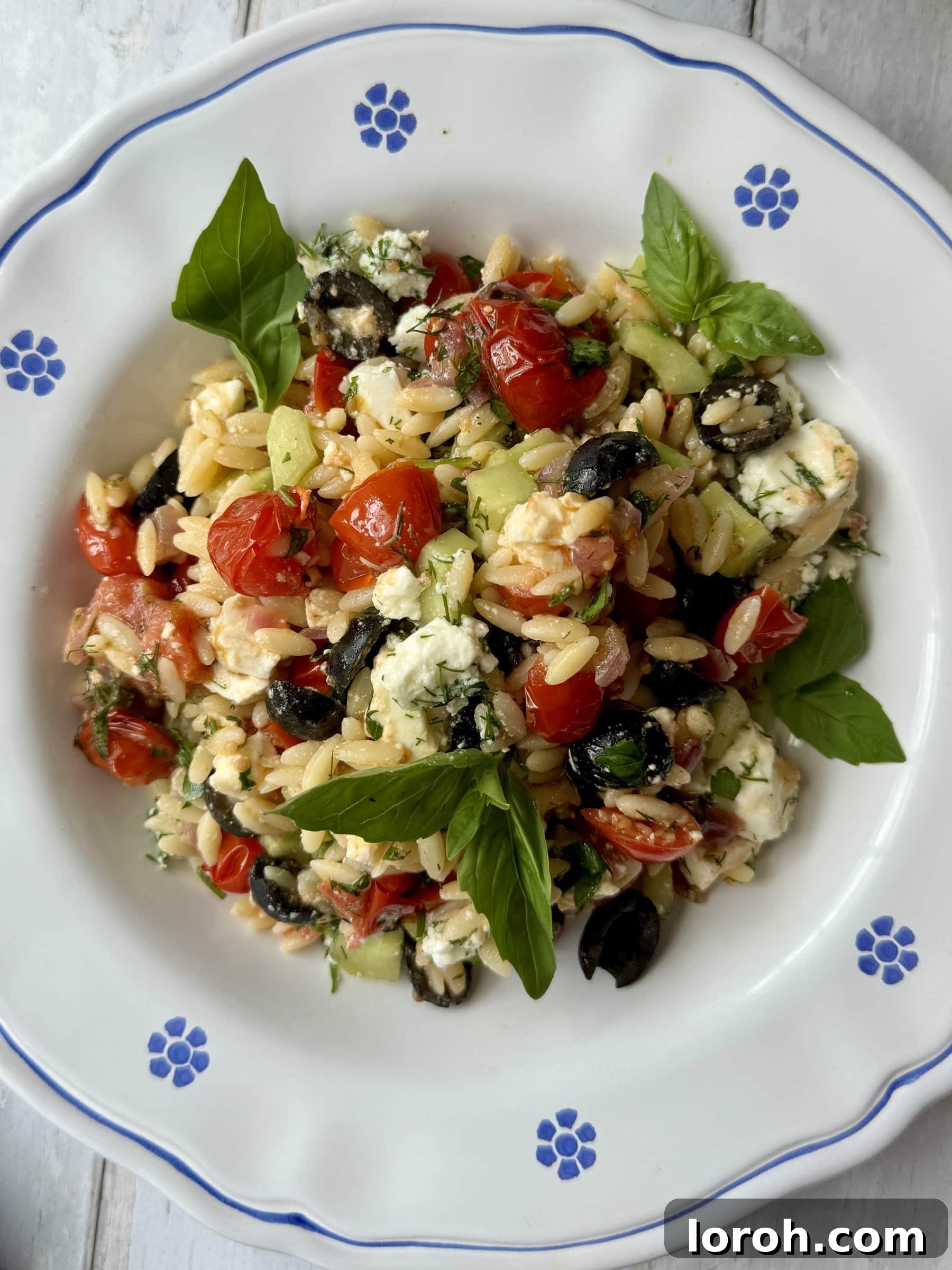 Vibrant Greek Orzo Salad 2 Delicious Greek pasta salad with orzo, feta, and olives in a white bowl with blue floral accents, ready to be served.