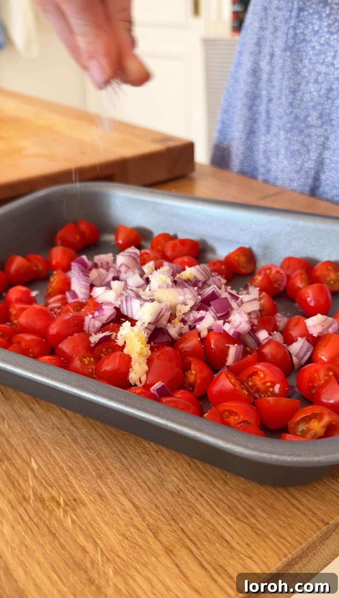 Vibrant Greek Orzo Salad 4 Cherry tomatoes, red onion, and garlic tossed with olive oil and seasoning on a baking tray, ready for roasting.