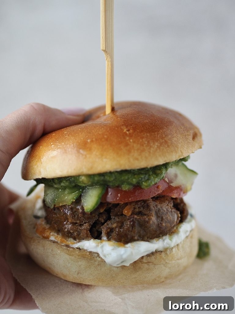 Lamb Burgers: A Fresh Mediterranean-Italian Blend 10 Hand holding a lamb burger in a brioche bun with salad, tzatziki and pesto.