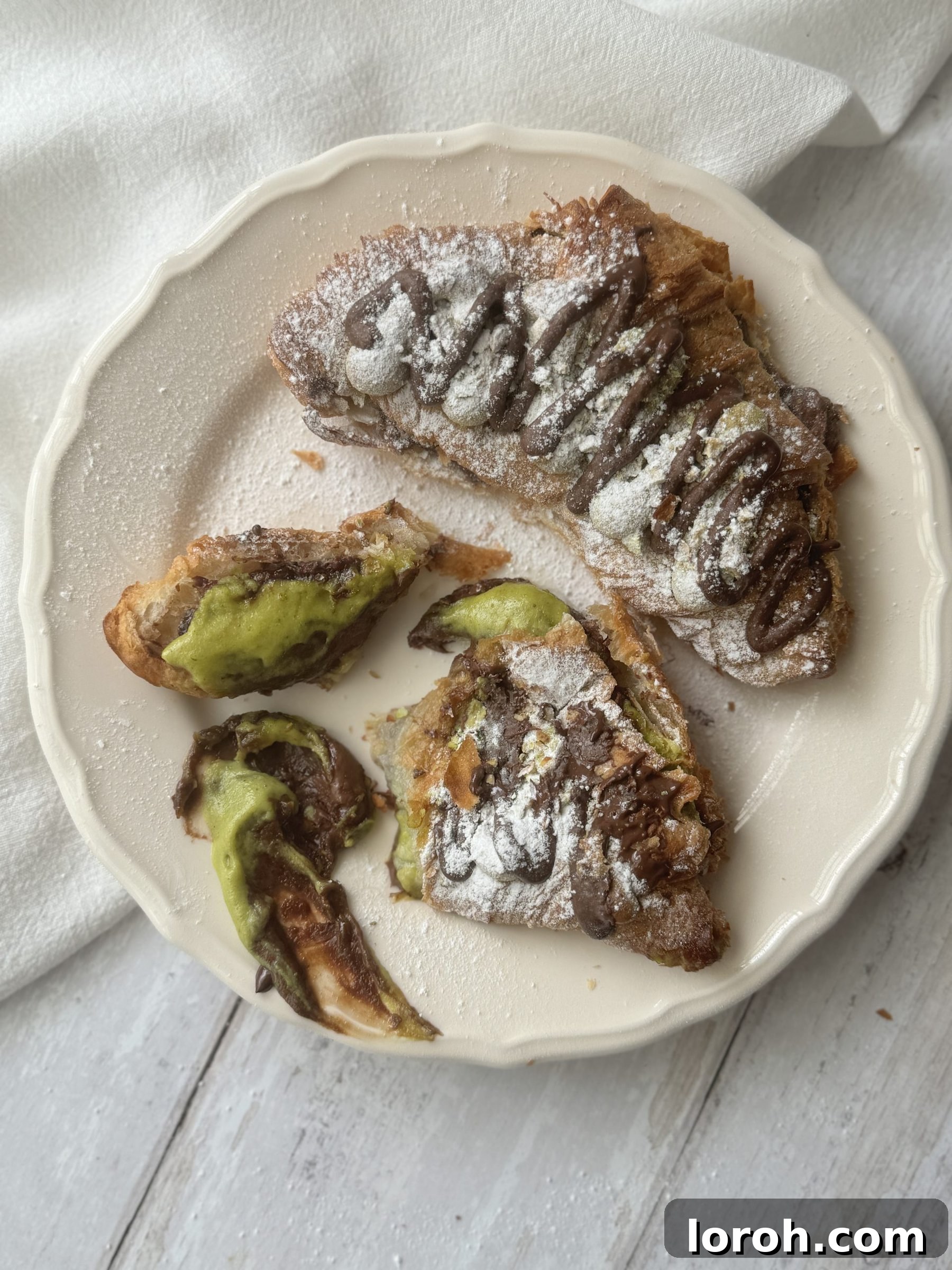 Handcrafted Pistachio Croissant with Rich Homemade Cream 3 Two beautifully presented pistachio croissants on a pristine white plate, showcasing their rich filling and inviting texture.