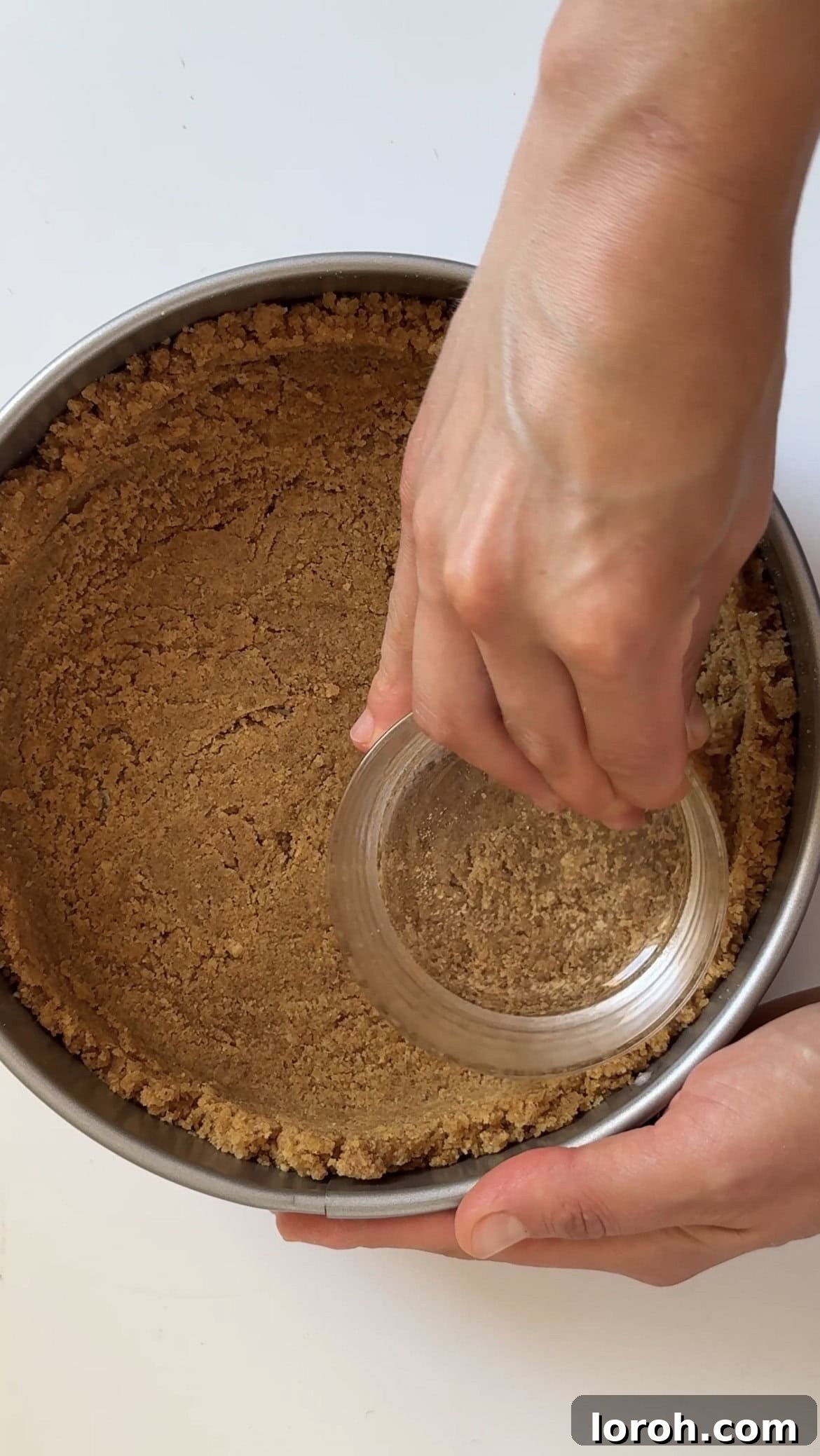 Golden Torched Cheesecake 5 A woman firmly pressing a biscuit crust into a springform pan using a glass.