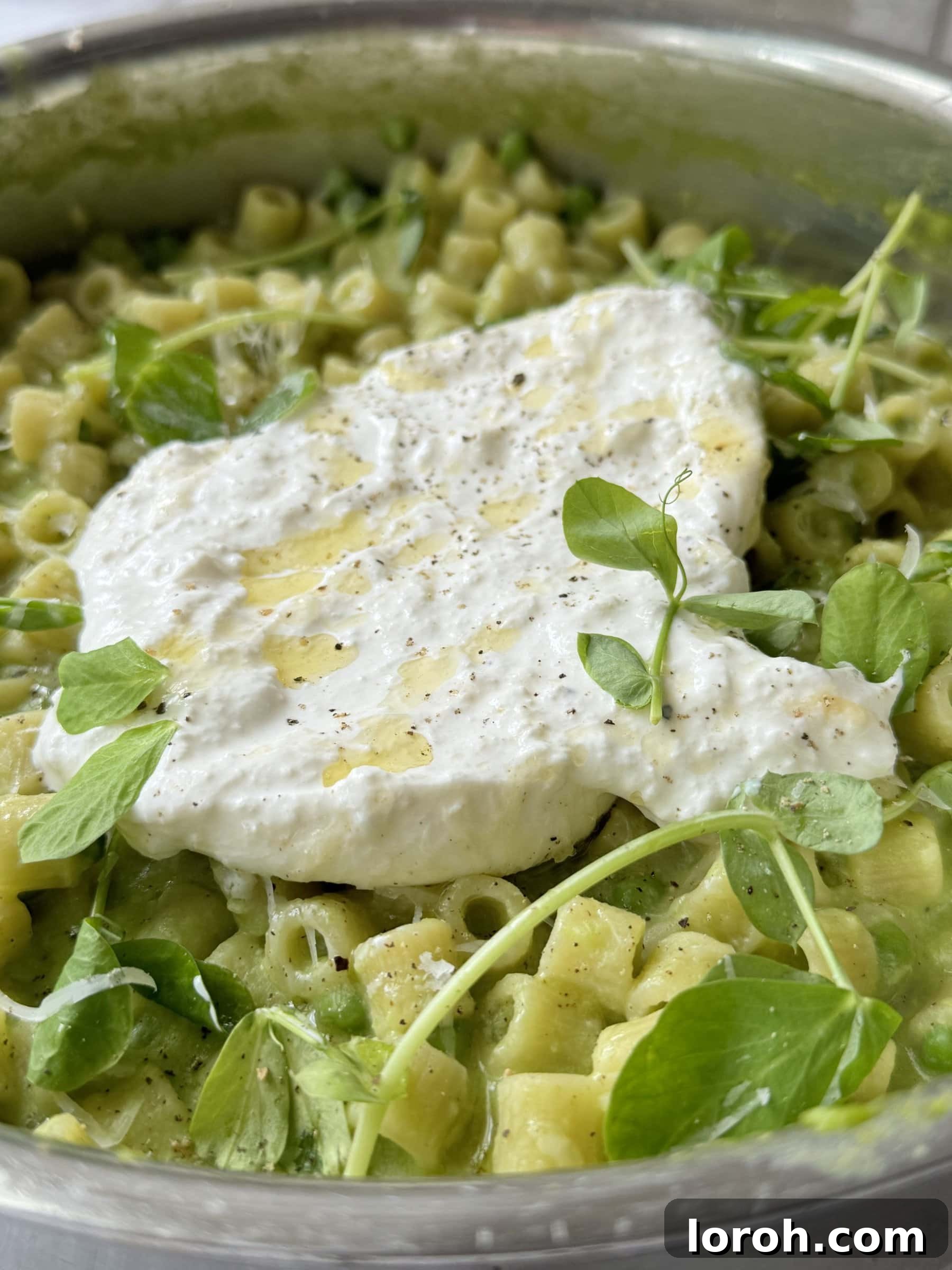 A vibrant close-up of the cooked one pan pasta and peas with melted burrata on top.