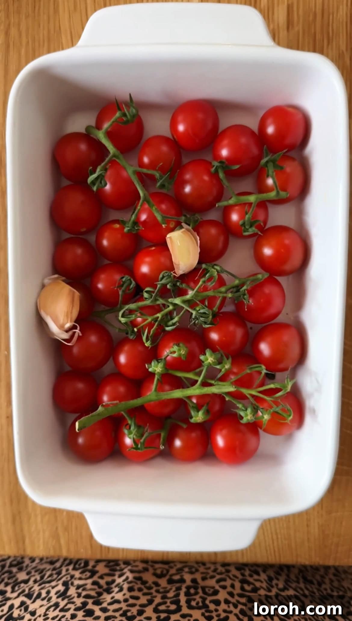 Tomato Butter: The Secret to Everything Delicious 4 Raw cherry tomatoes, unpeeled garlic cloves, and a drizzle of olive oil in a white ovenproof dish, ready for roasting.