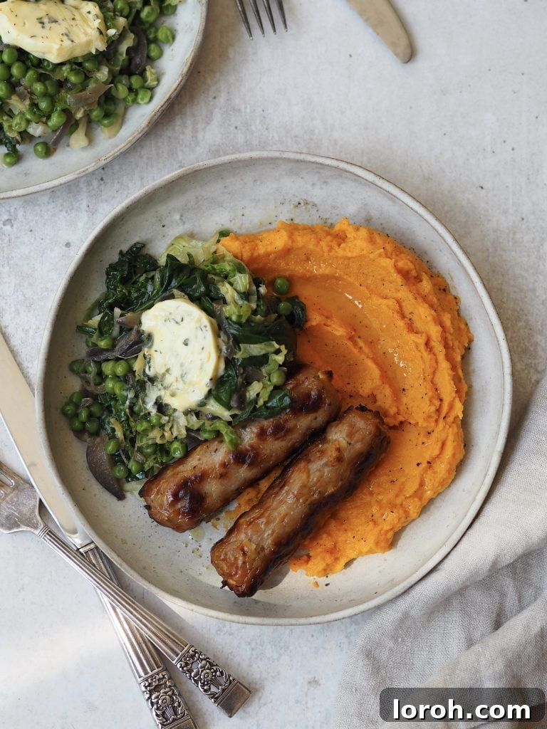Grey plate of sweet potato mash, roasted sausages, wilted greens and garlic butter.