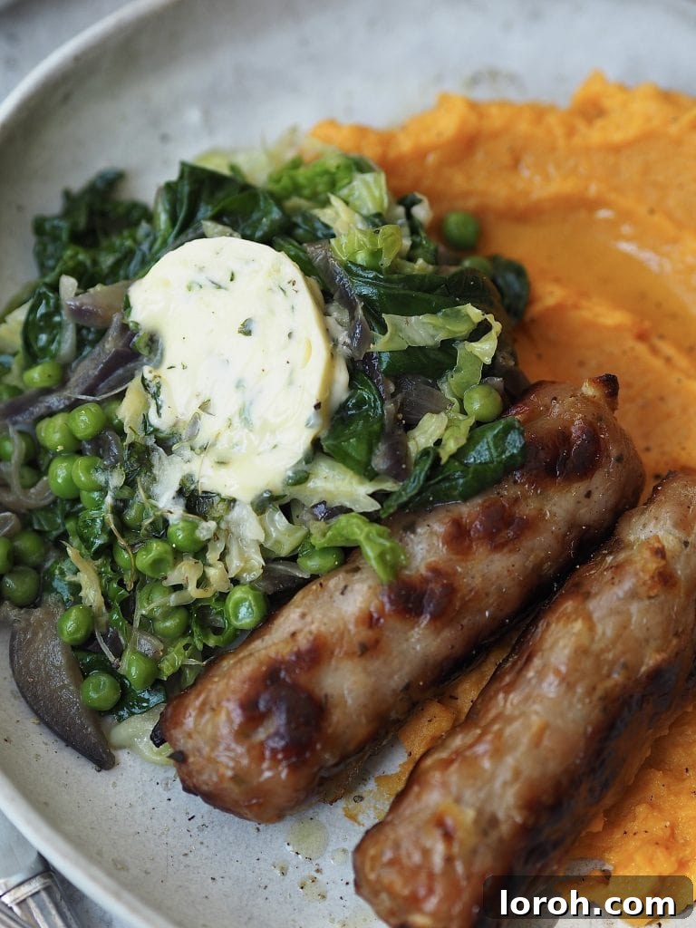 Close up of roasted sausages served with greens topped with garlic butter and some mashed sweet potato.