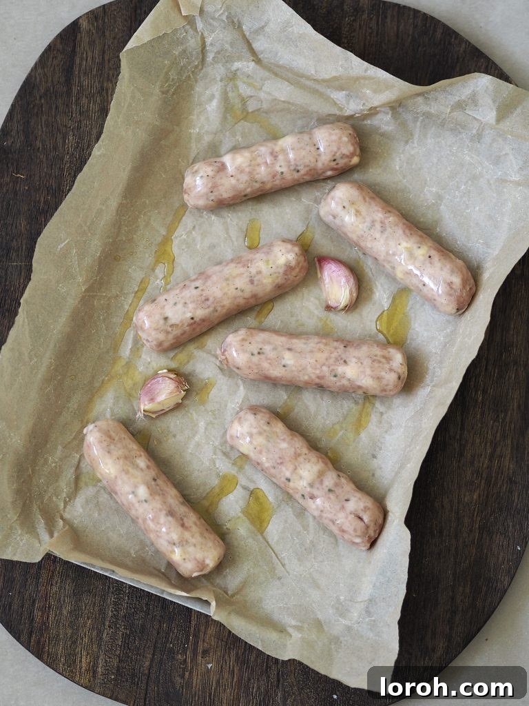 Sausages and whole garlic cloves drizzled with oil on a baking parchment lined baking tray.