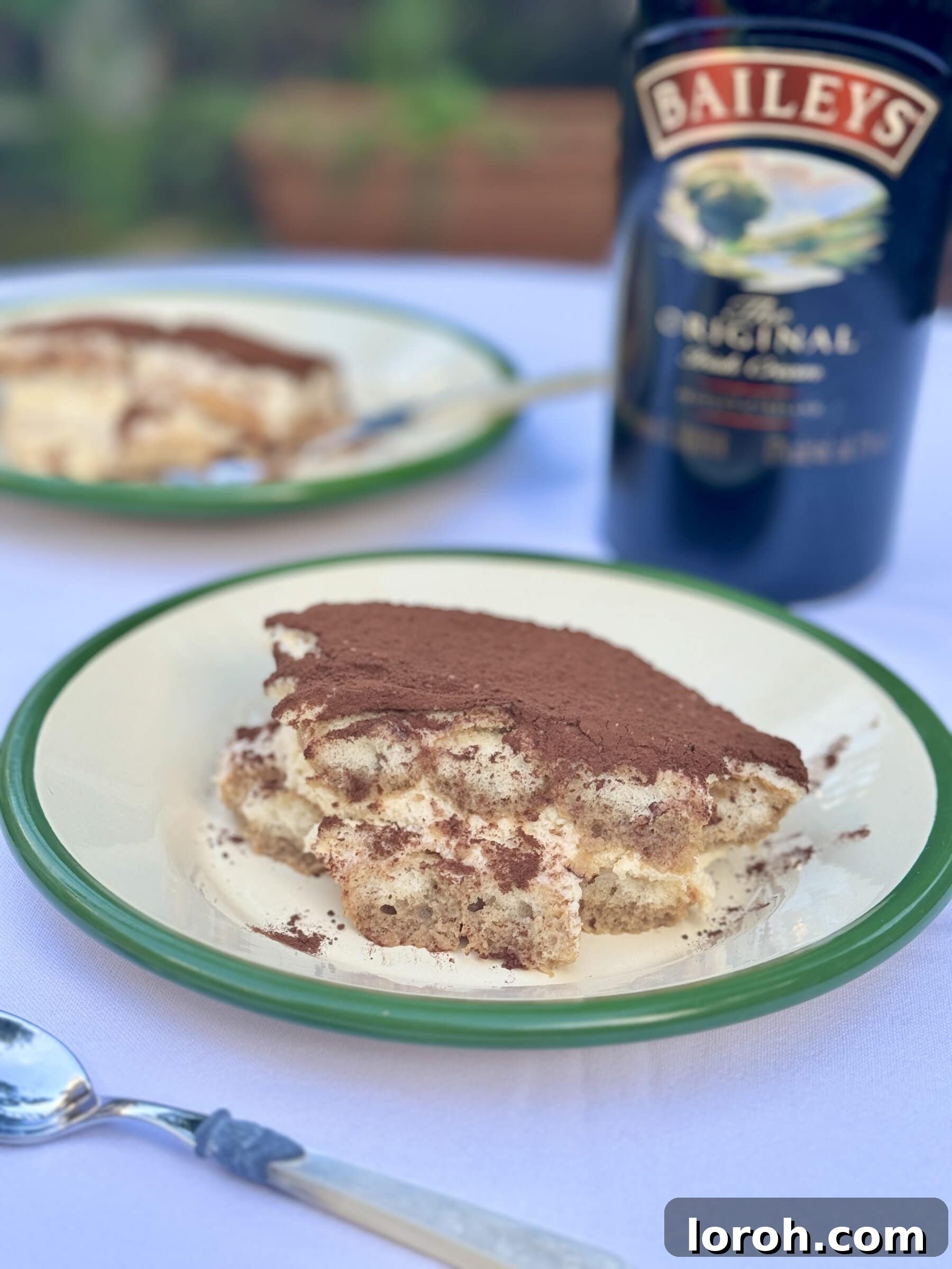 A slice of Baileys Tiramisu on a white plate, showcasing its distinct layers and dusting of cocoa.
