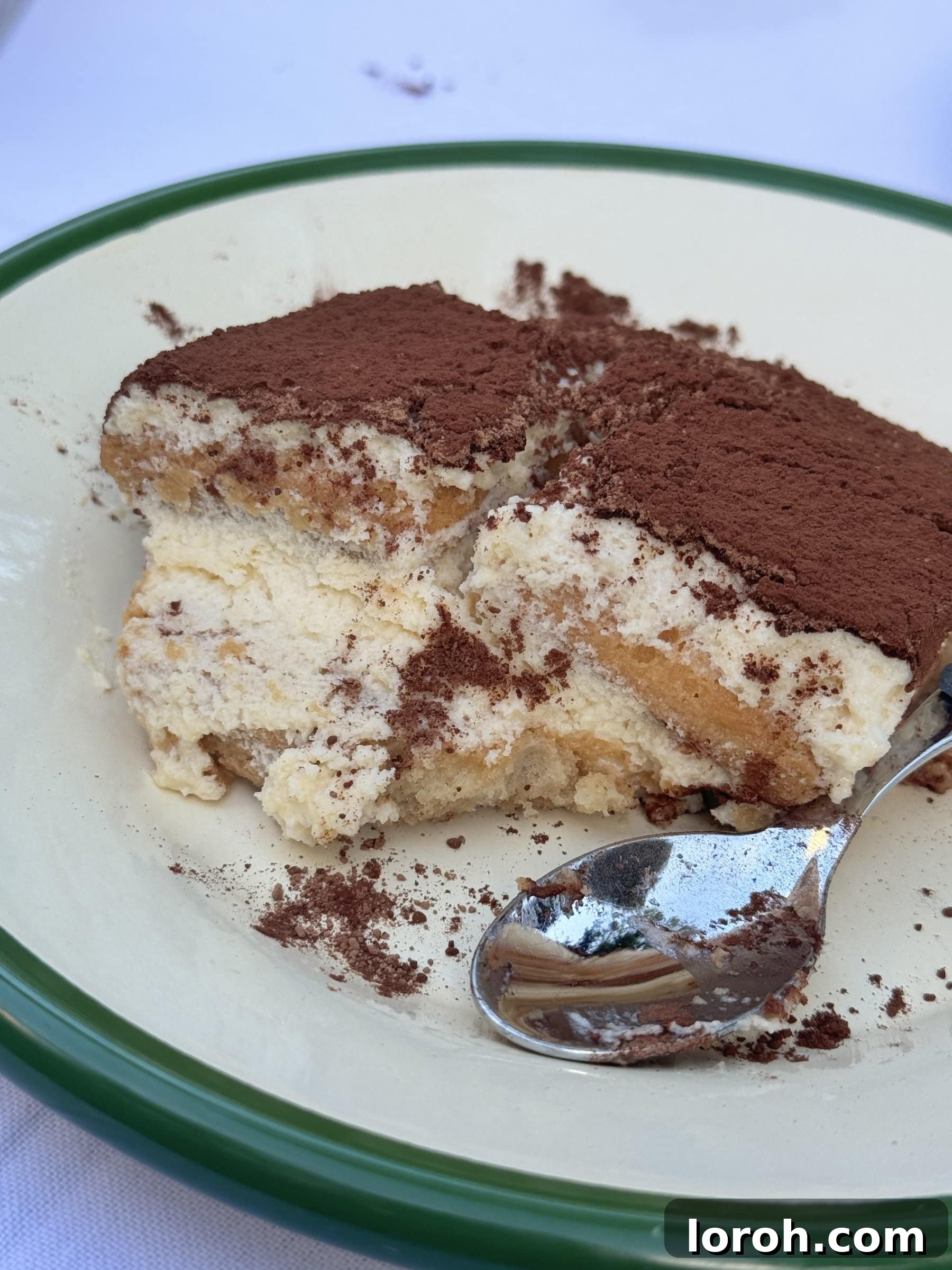 A serving of Baileys Tiramisu on a plate, with a spoon ready to scoop into its creamy layers.