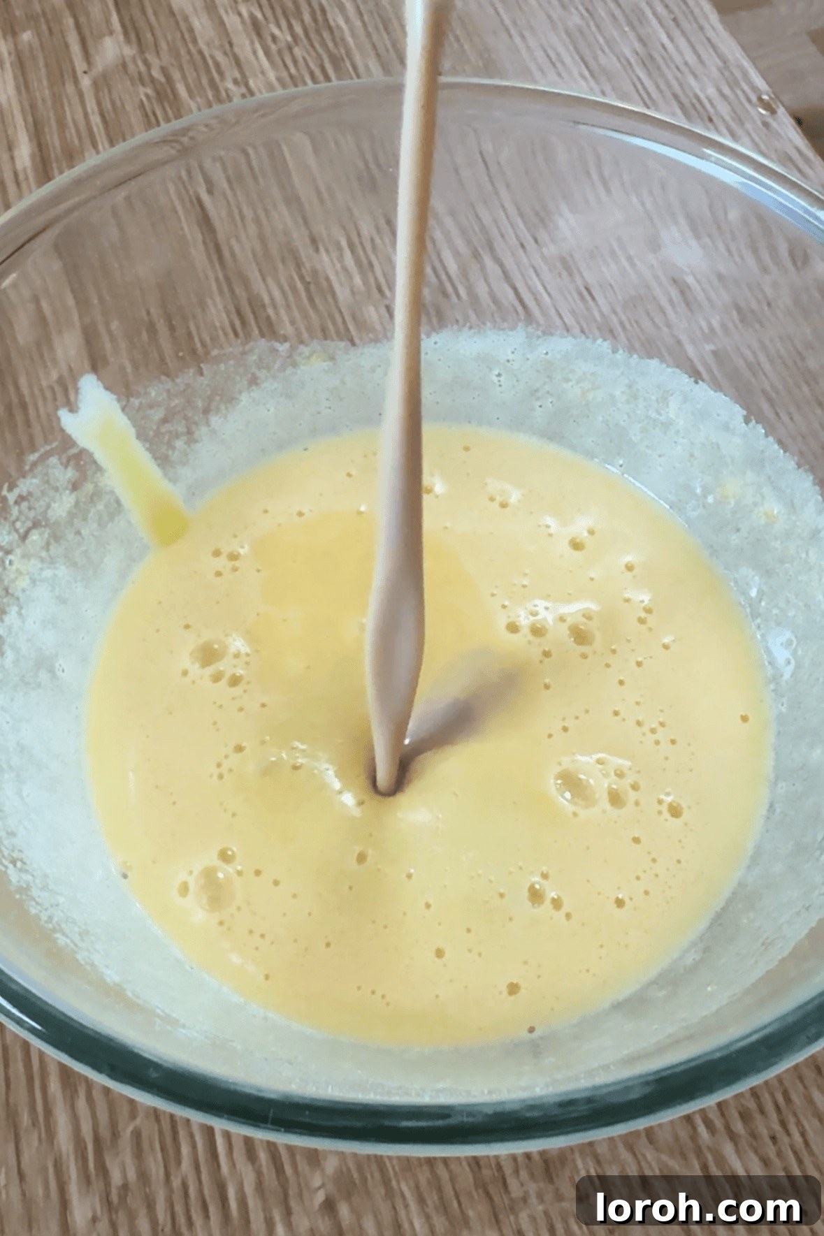 Adding Baileys Irish cream to the freshly whisked egg yolk and sugar mixture in a bowl.