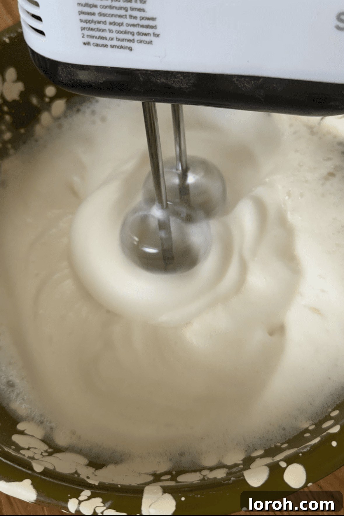 Whisking egg whites to stiff peaks using an electric whisk, demonstrating proper aeration.