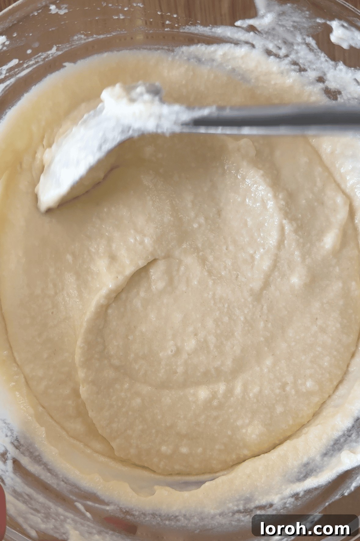 Gently folding whisked egg whites into the mascarpone cream mixture using a spatula.