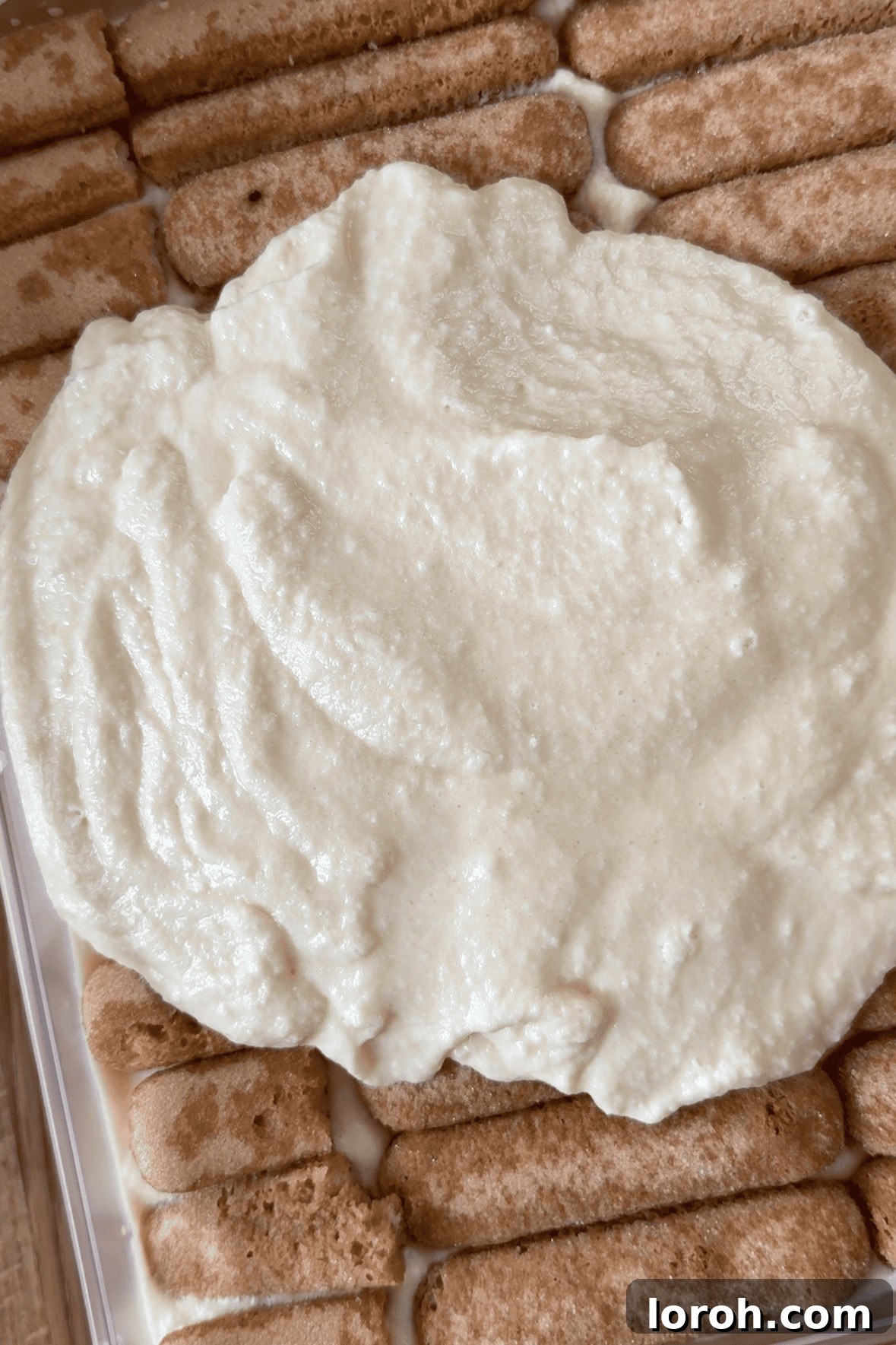 Spreading a smooth, even layer of Baileys mascarpone cream over the first layer of soaked ladyfingers in a dish.