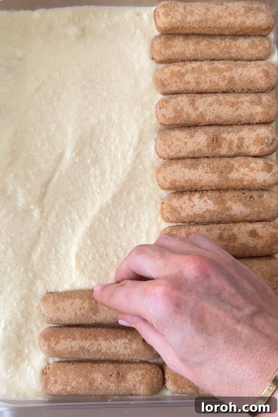 Adding a second layer of coffee and Baileys soaked ladyfingers to the partially assembled tiramisu.