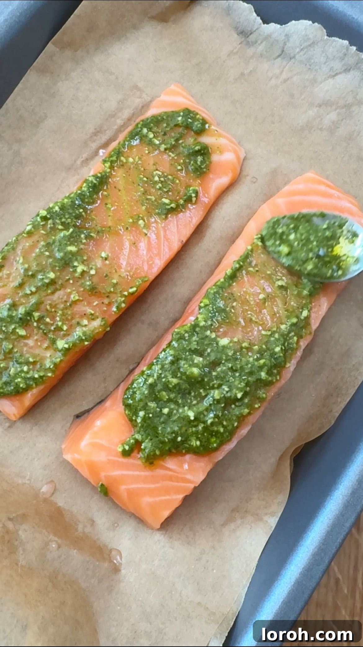 Applying pesto generously onto a salmon fillet on a baking sheet.