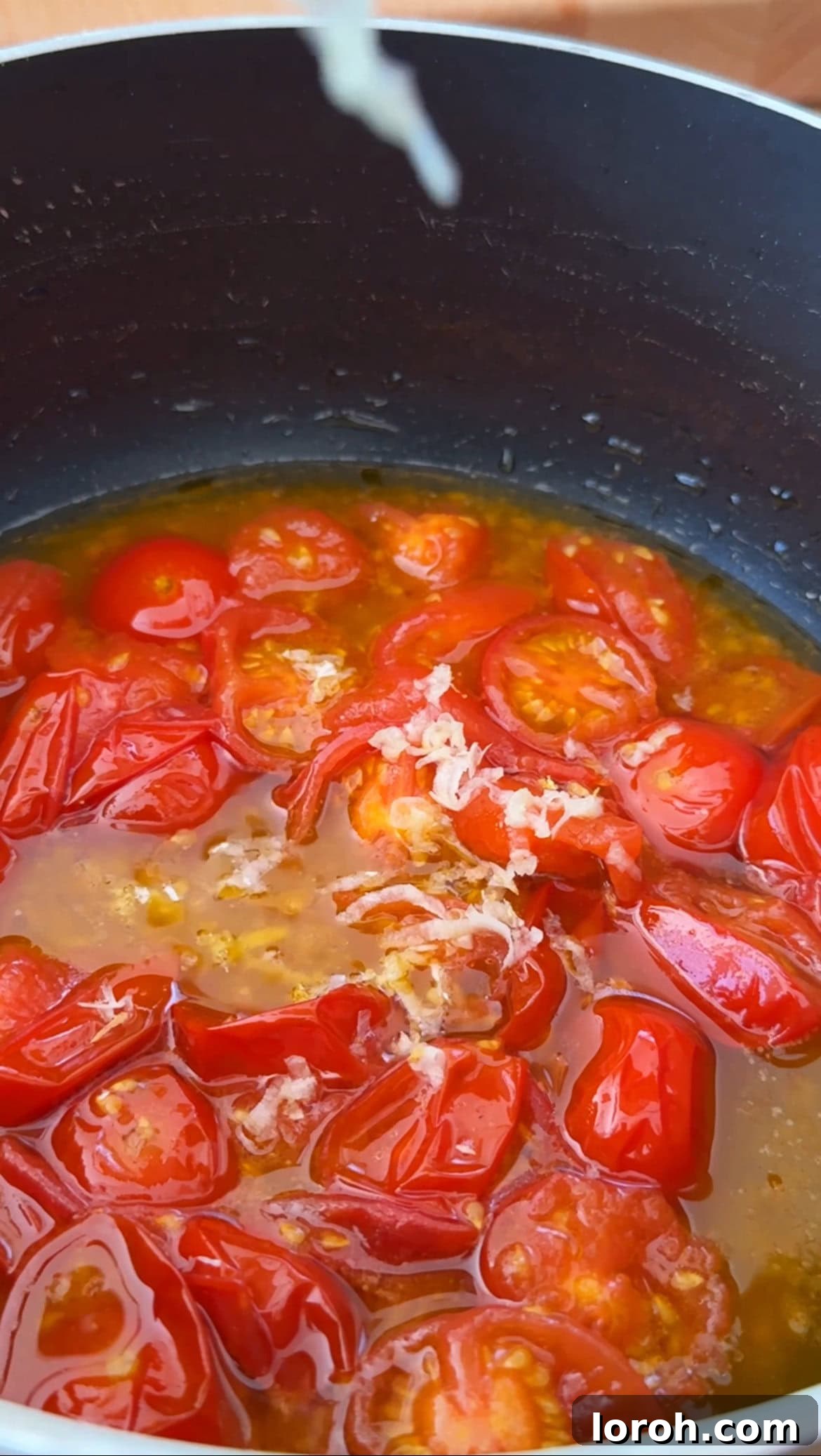 Softened cherry tomatoes being gently squashed in a pan to create a dressing.